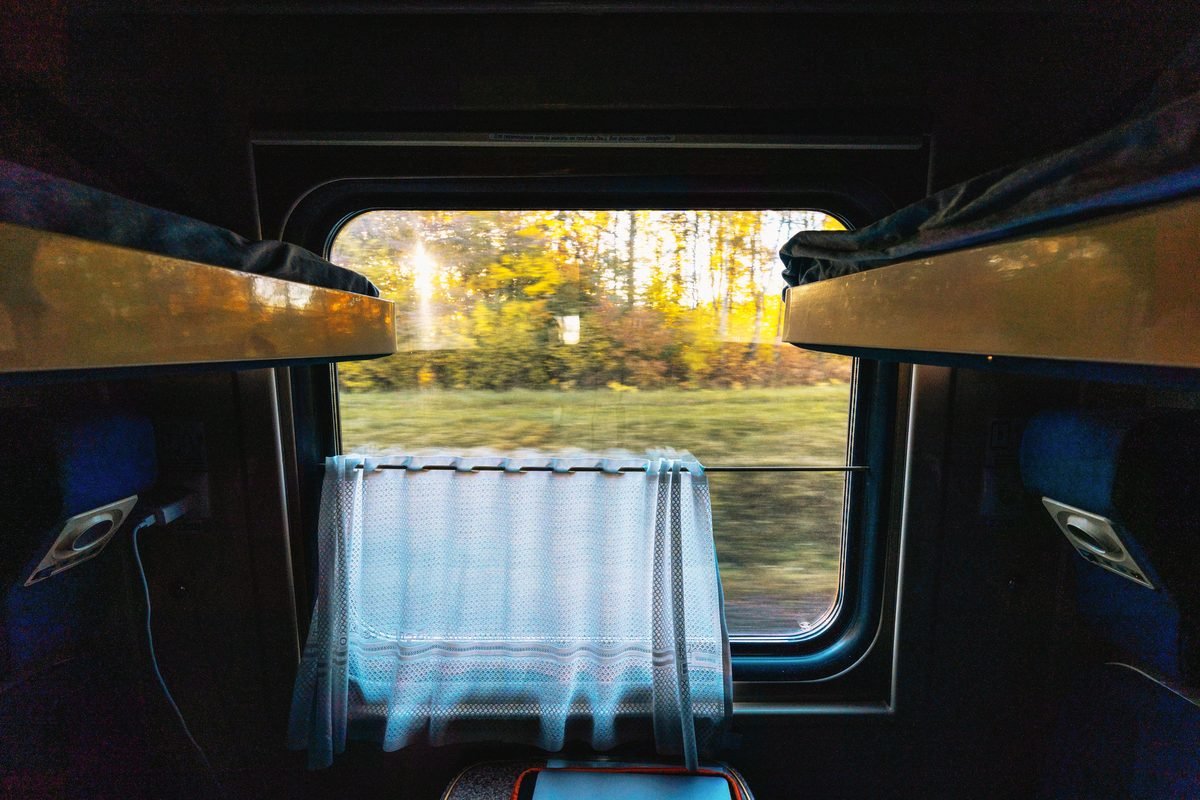 Interior view of a train sleeper cabin looking out at an autumn landscape.