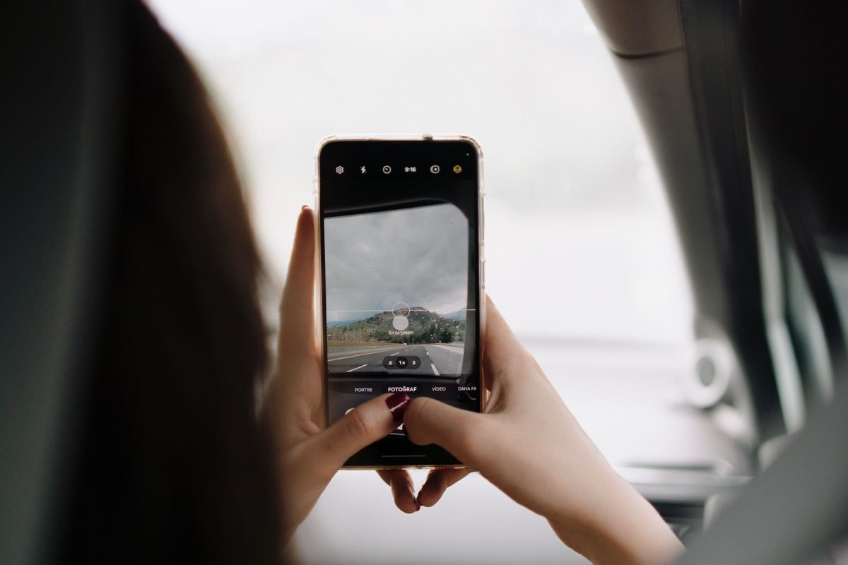 A person using a smartphone to photograph a scenic view through a vehicle window.