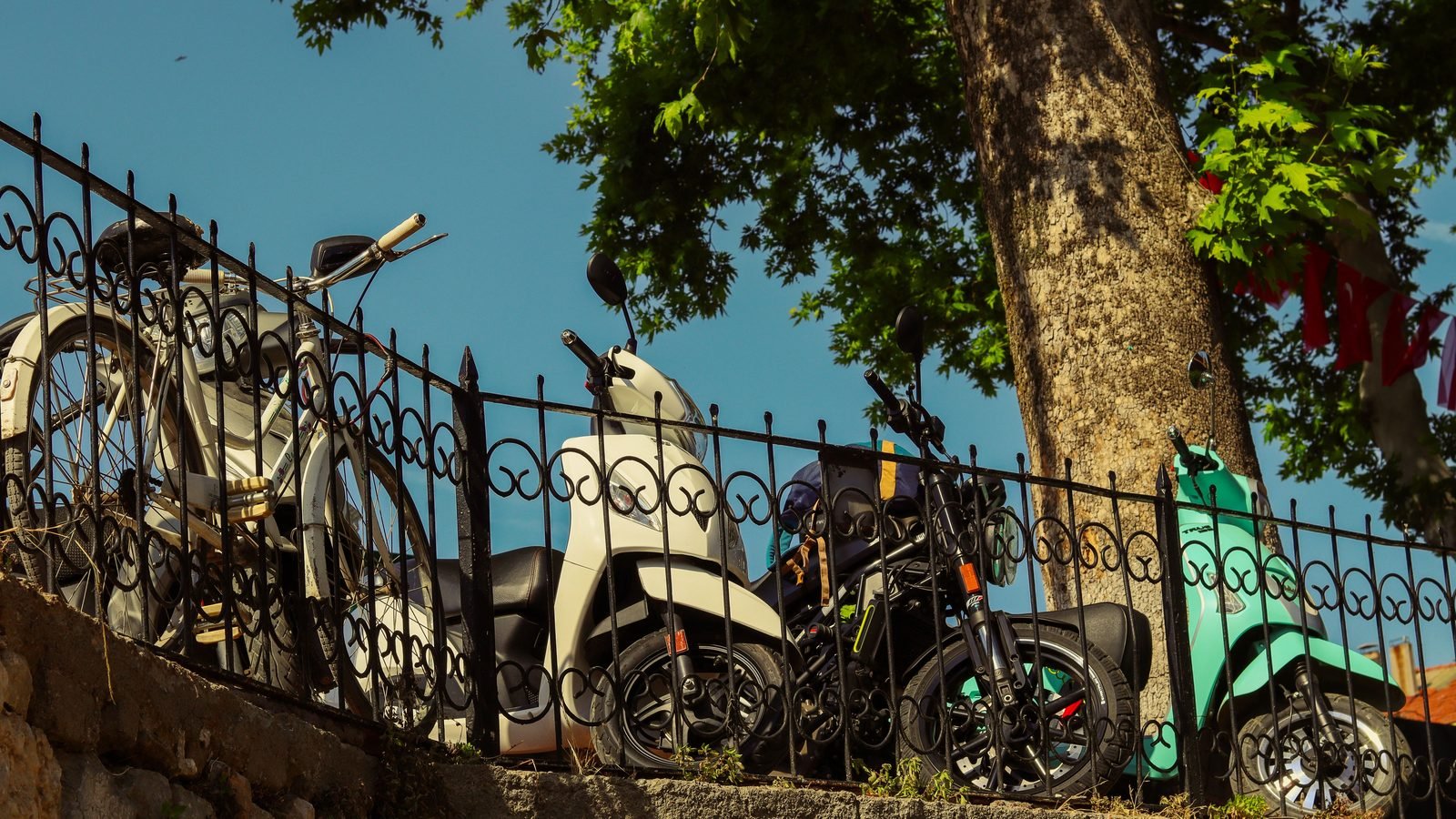Scooters and bicycle parked against a decorative metal fence