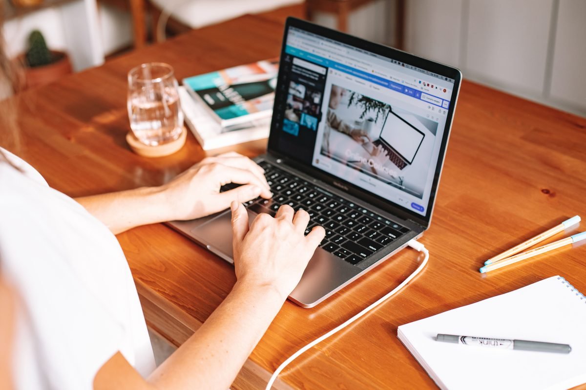 Person working remotely on a laptop at a wooden desk