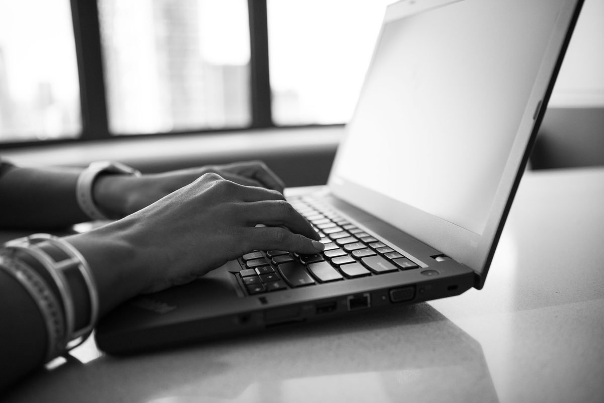 Black and white close-up of hands typing on a laptop