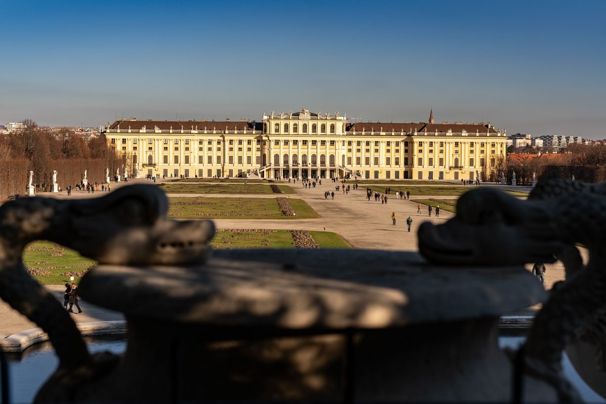 Schonbrunn Palace viewed across its symmetrical gardens under a clear blue sky.