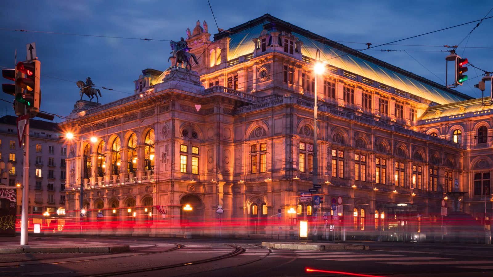Illuminated Vienna State Opera House at night with light trails from passing traffic.