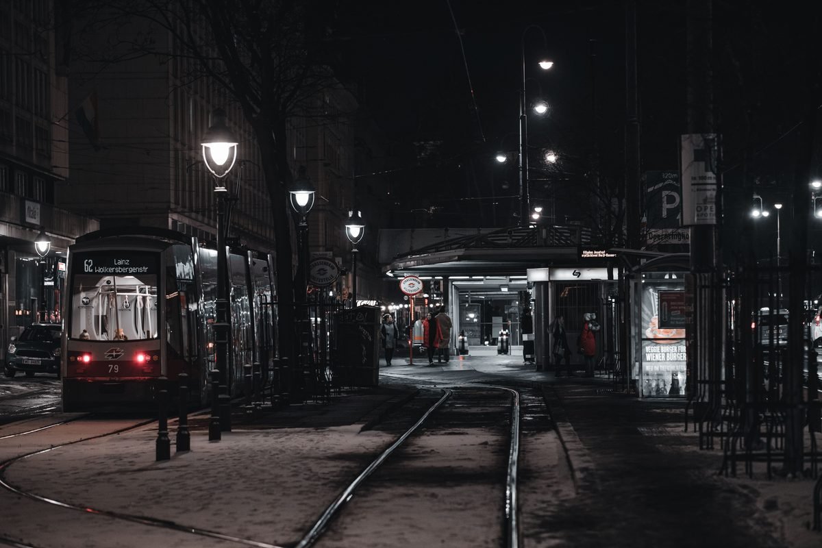 A modern tram stopping at a station on a snowy winter night in Vienna.
