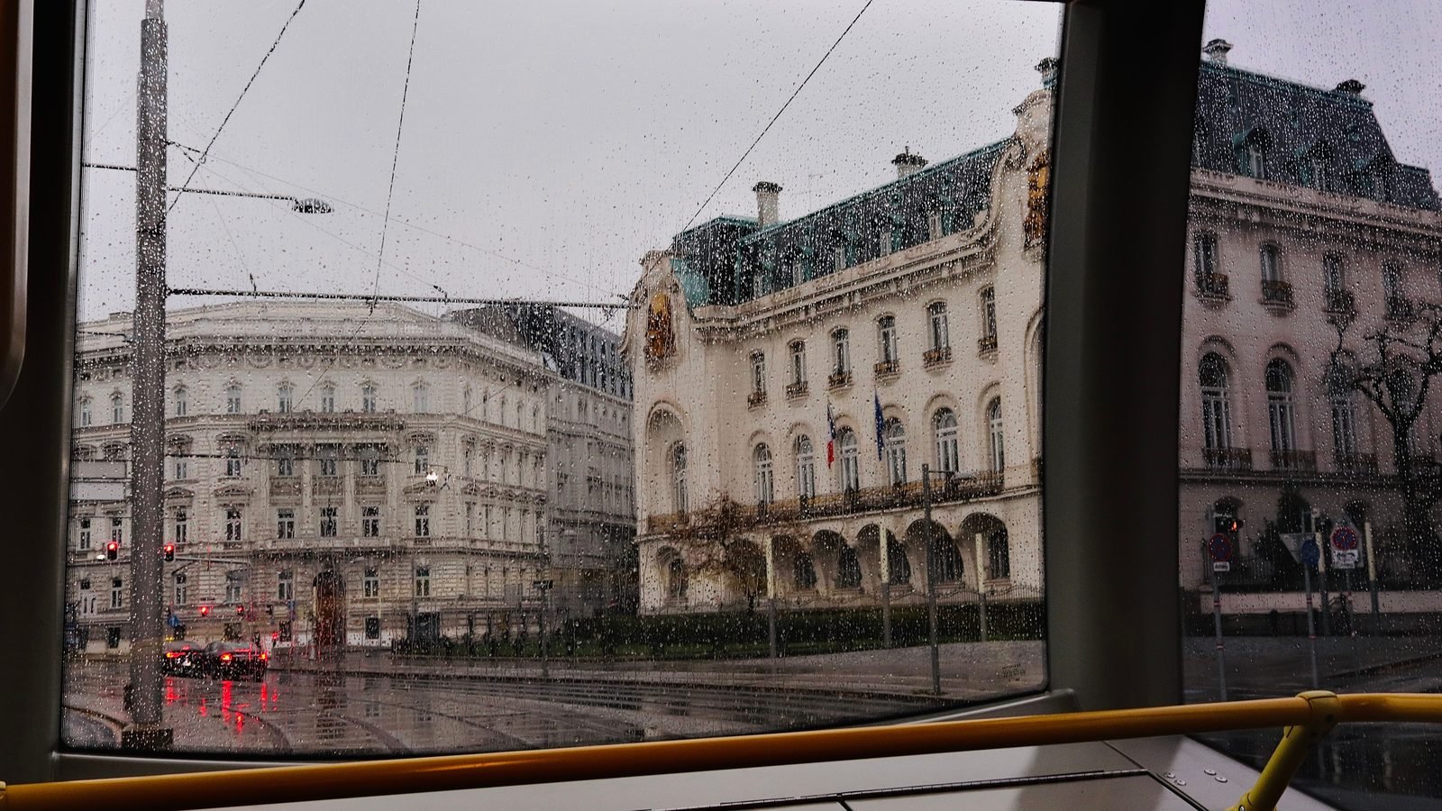 Historic Vienna buildings seen through rainy tram windows during a commute.