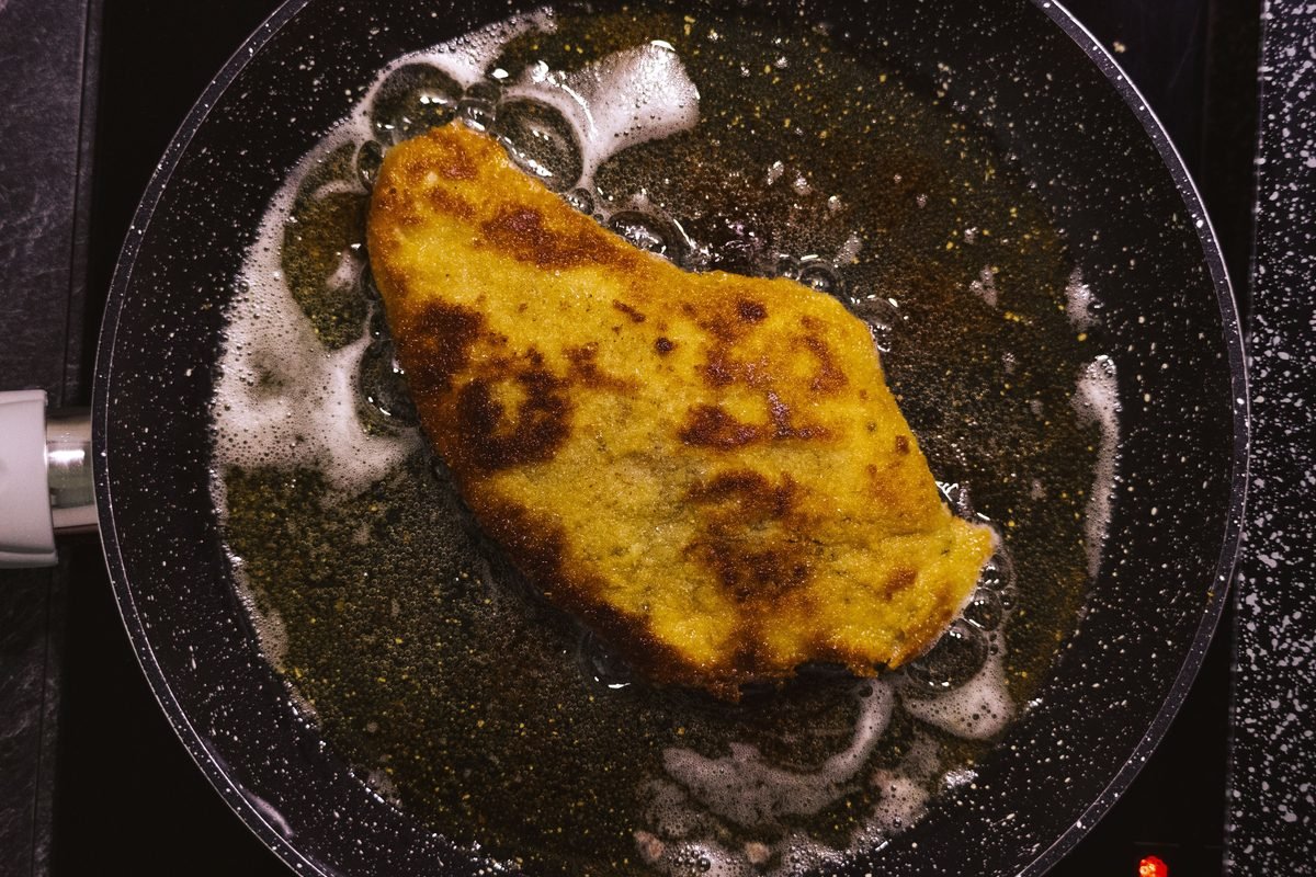 A golden-brown schnitzel frying in a hot skillet.