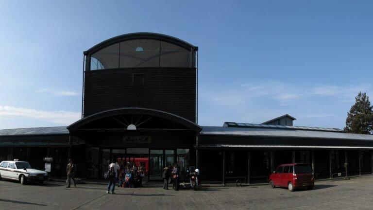 Panoramic exterior view of Yufuin Station building with dark wooden architecture on a clear sunny day