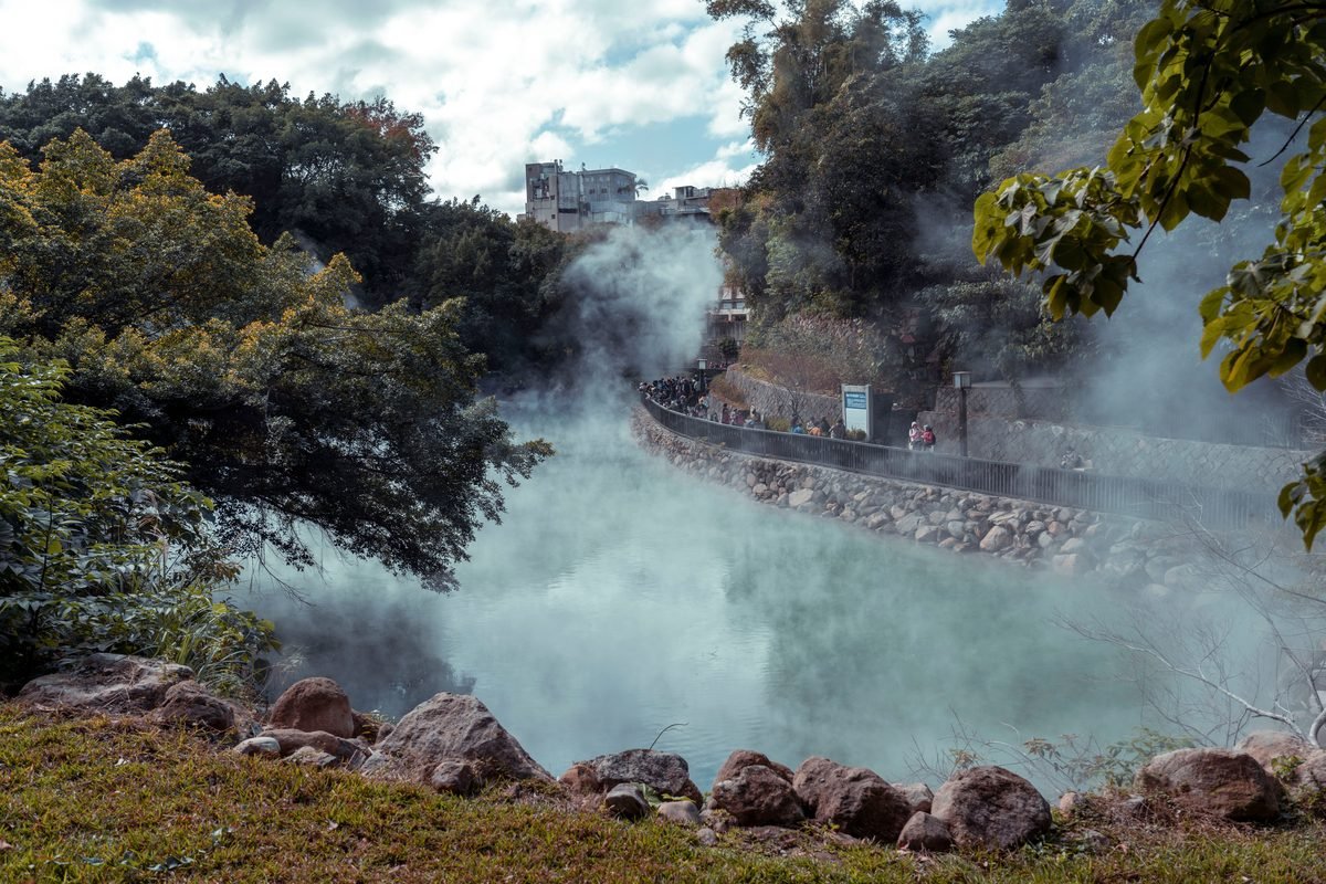 Steaming turquoise thermal water flowing along a stone-lined channel surrounded by trees