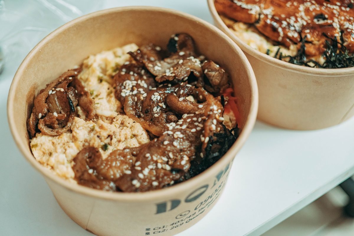 Takeout bowl filled with tender sliced meat and rice garnished with sesame seeds