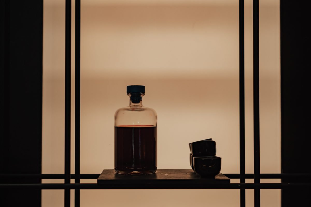 Moody still life featuring a bottle and cups on a shelf.