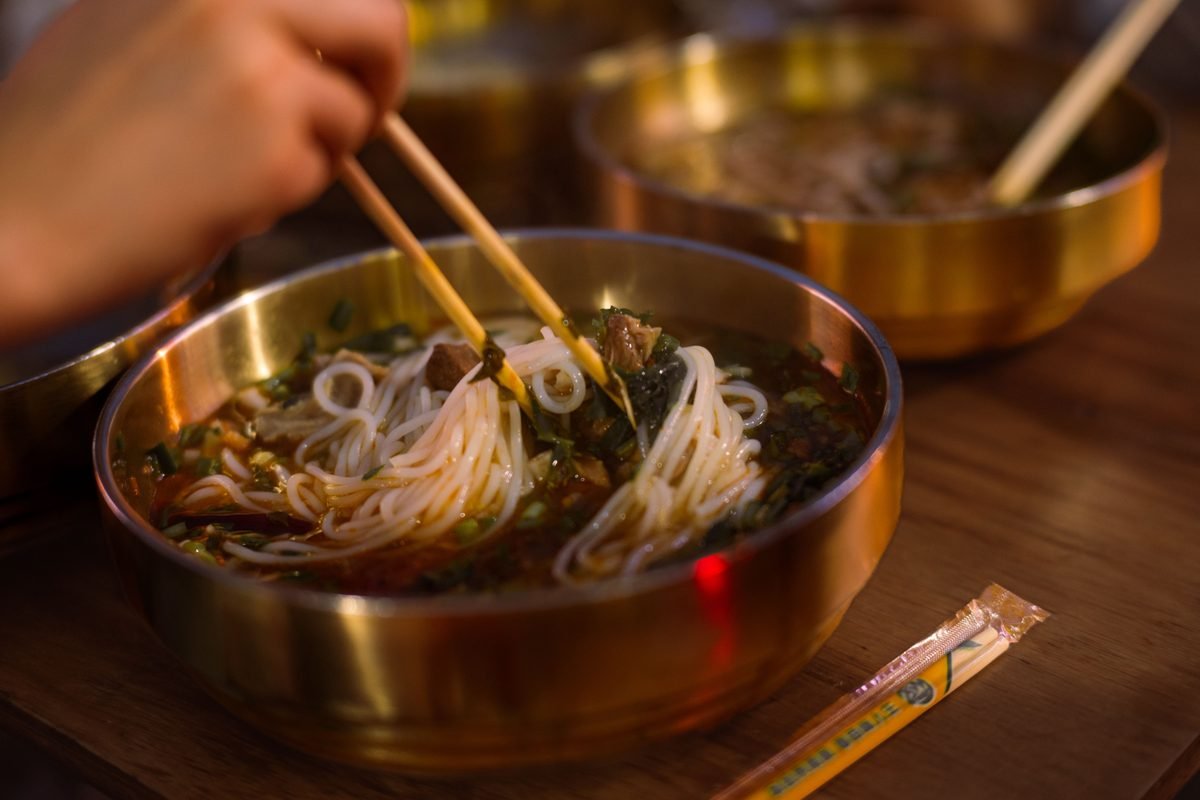 Noodles served in a traditional brass bowl with chopsticks