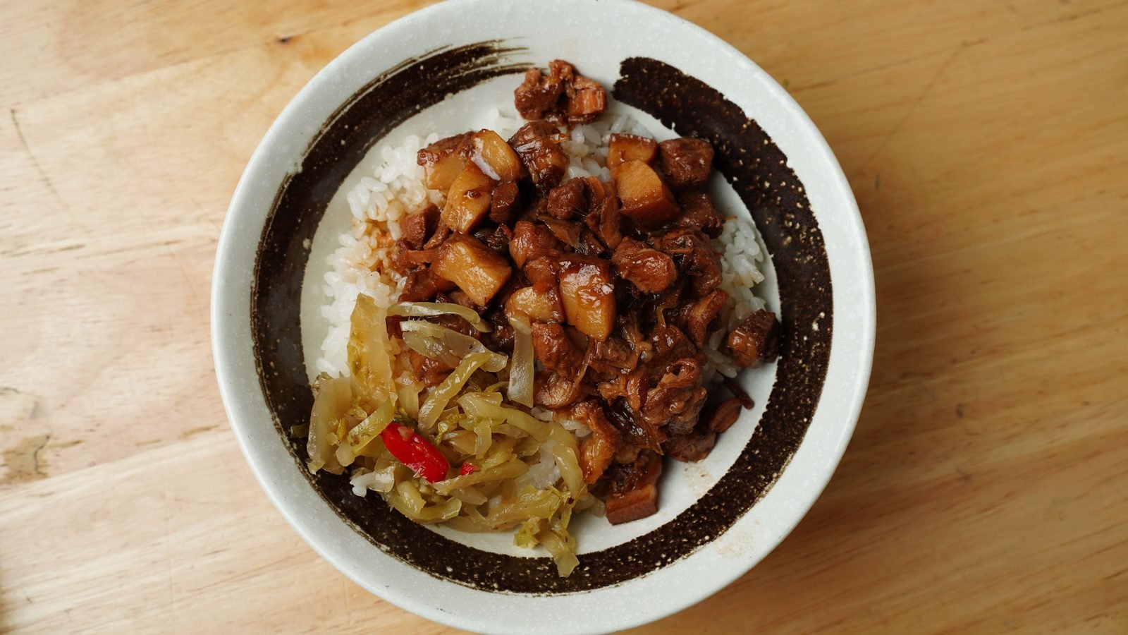A savory bowl of braised pork and rice on a wooden table.