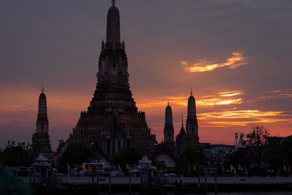Wat Arun temple silhouetted against sunset over the river.