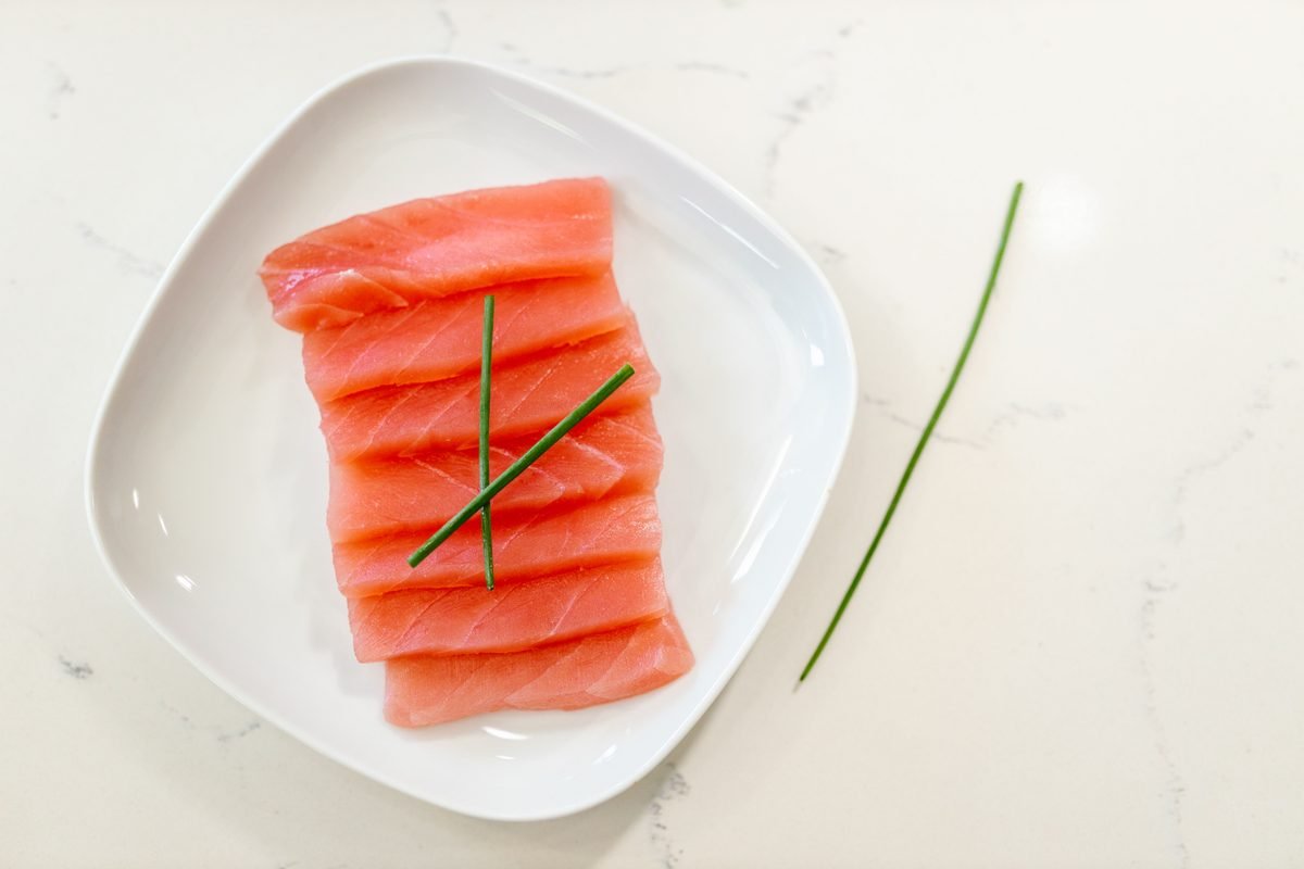 Sliced salmon sashimi on a white plate with chives