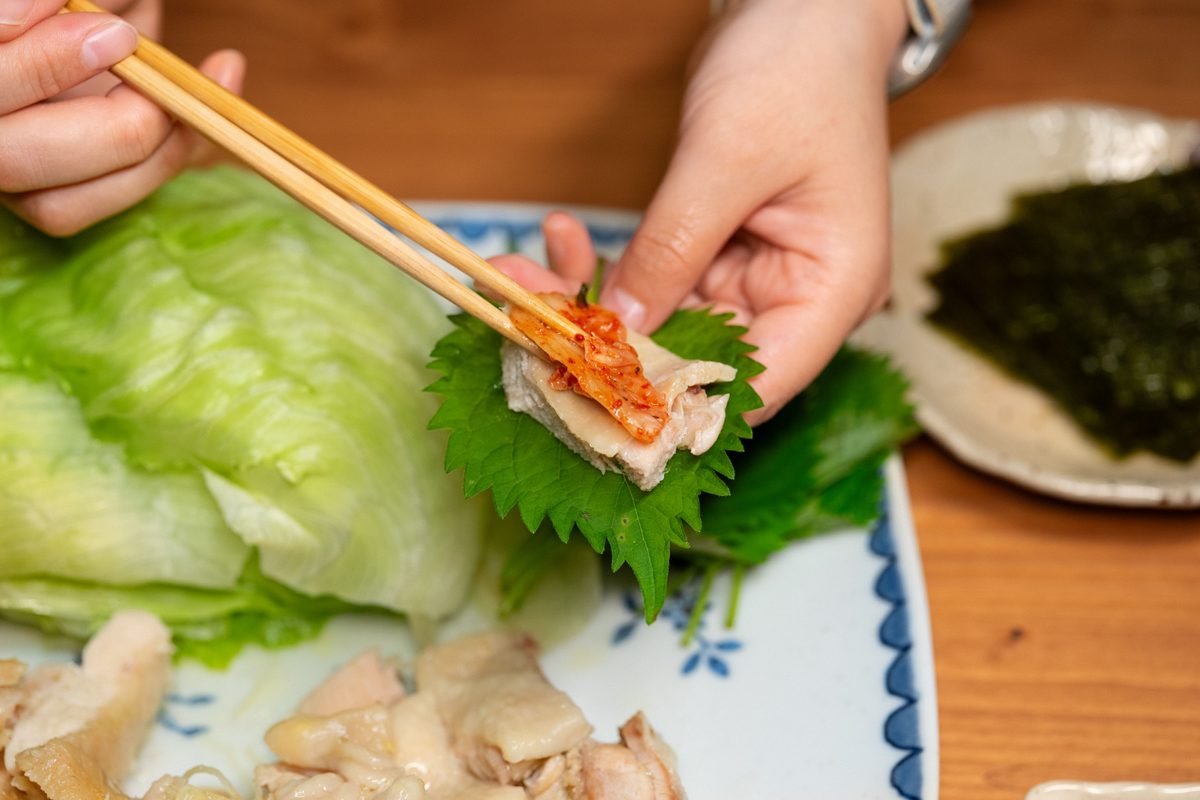 Person wrapping meat and kimchi in a perilla leaf with chopsticks