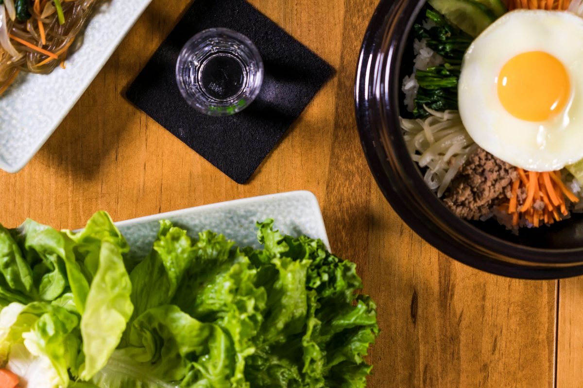 Korean bibimbap in a ceramic bowl with fresh ingredients on a wooden table