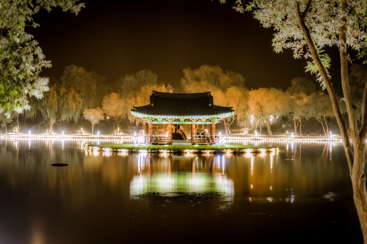 Illuminated traditional Asian gazebo at night surrounded by water