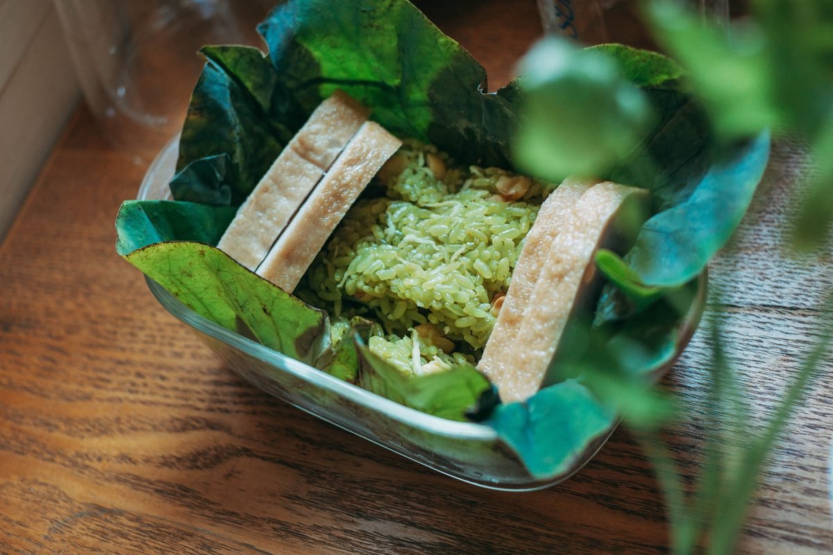 Green rice dish wrapped in lotus leaves served in a glass container