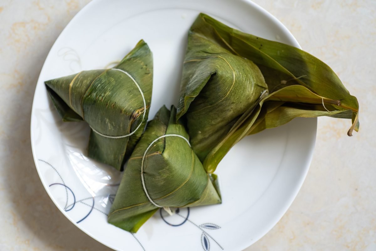 Three traditional leaf-wrapped rice dumplings served on a white plate.