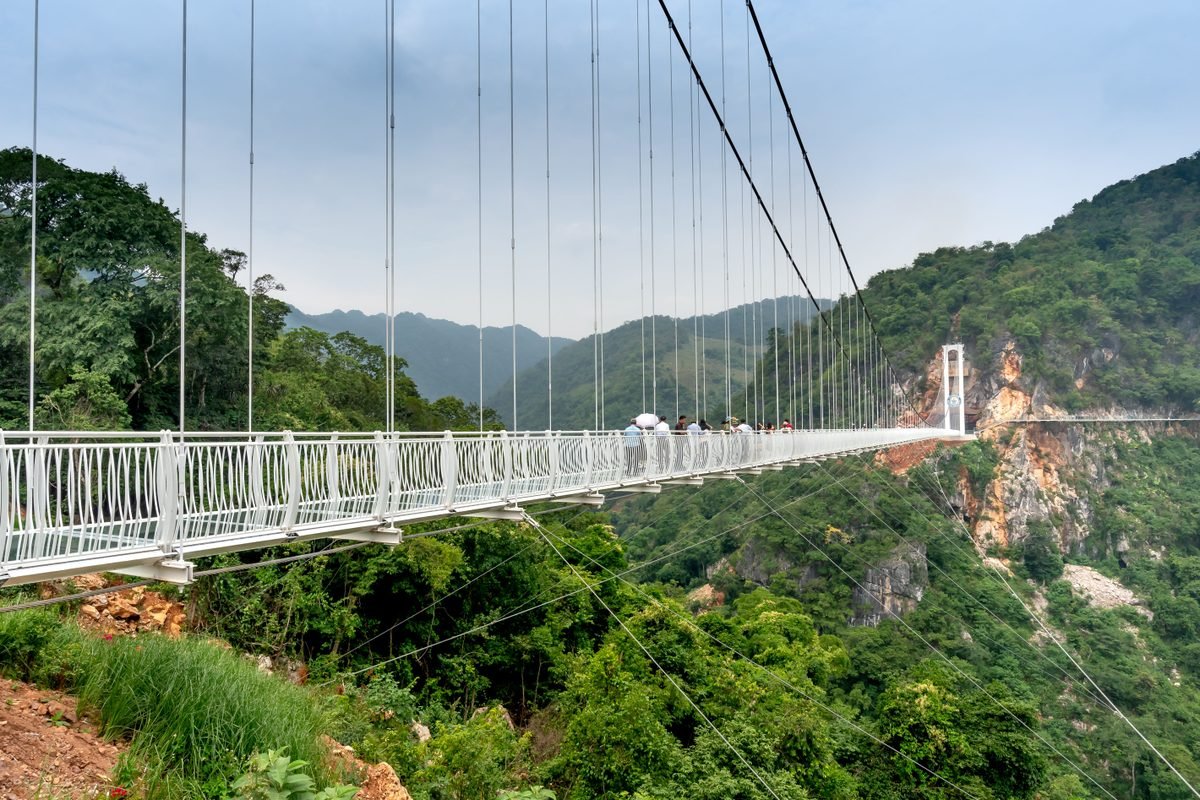 Long suspension bridge stretching across a verdant valley with mountains