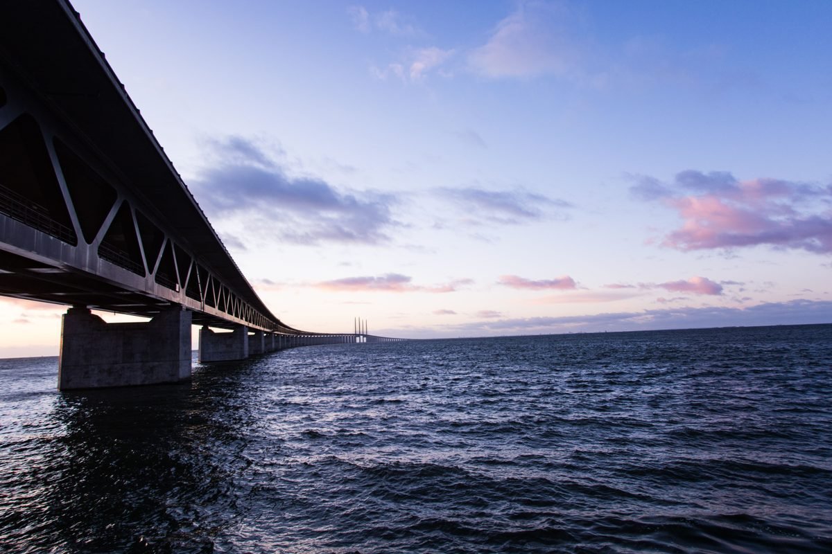 A long steel suspension bridge stretching over open water at sunset