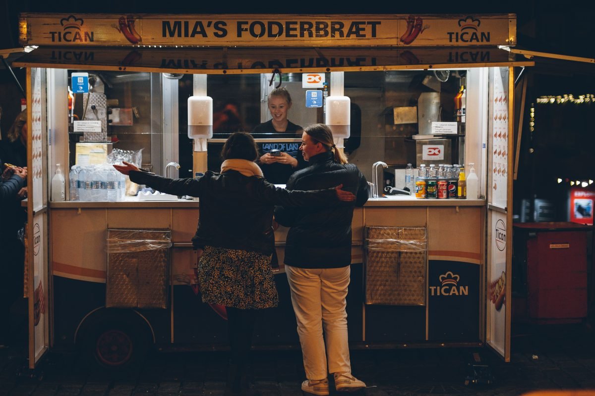 People purchasing food from a lighted street kiosk during evening hours