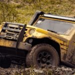 A yellow 4x4 SUV driving through a muddy off-road path