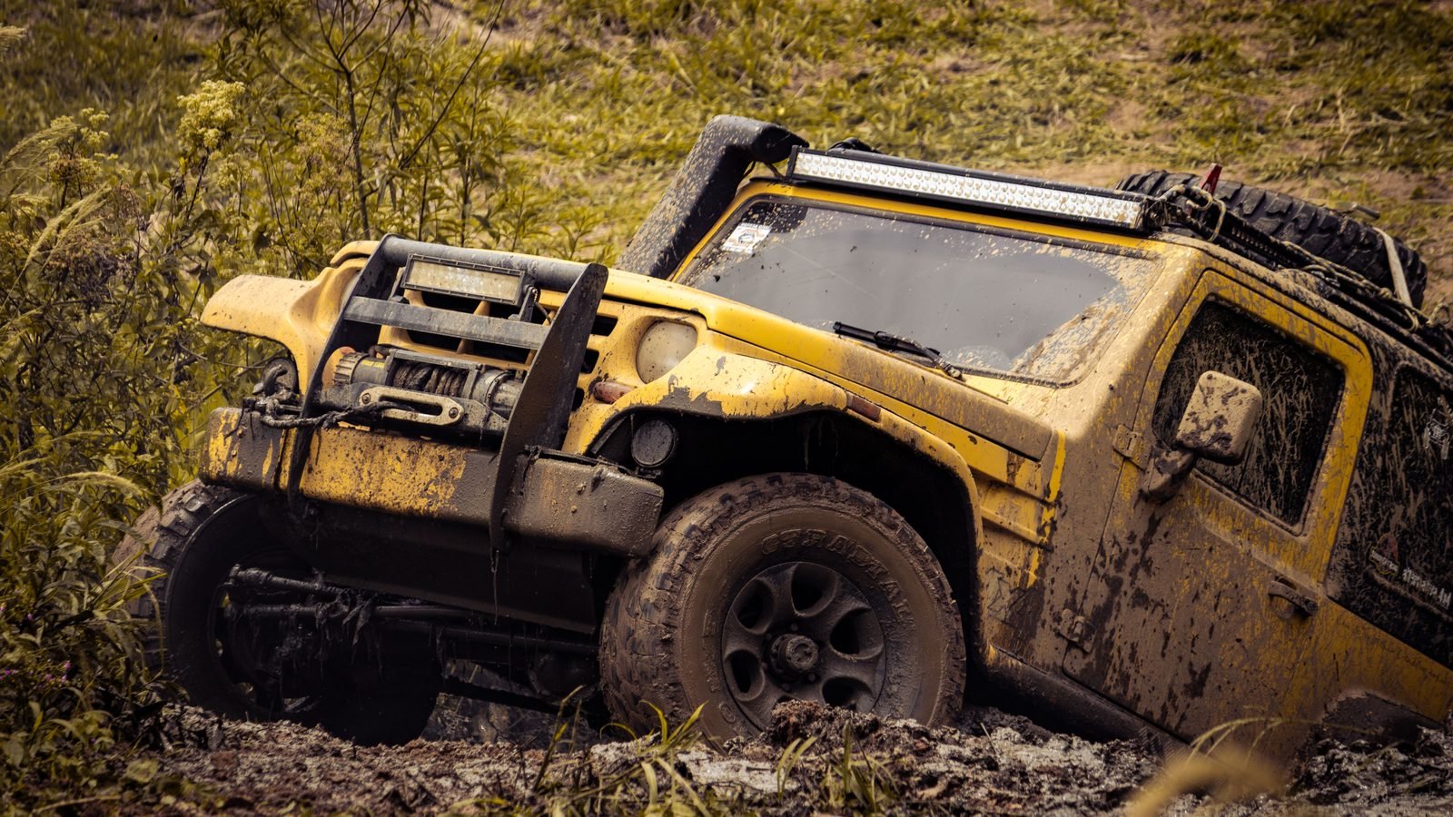 A yellow 4x4 SUV driving through a muddy off-road path