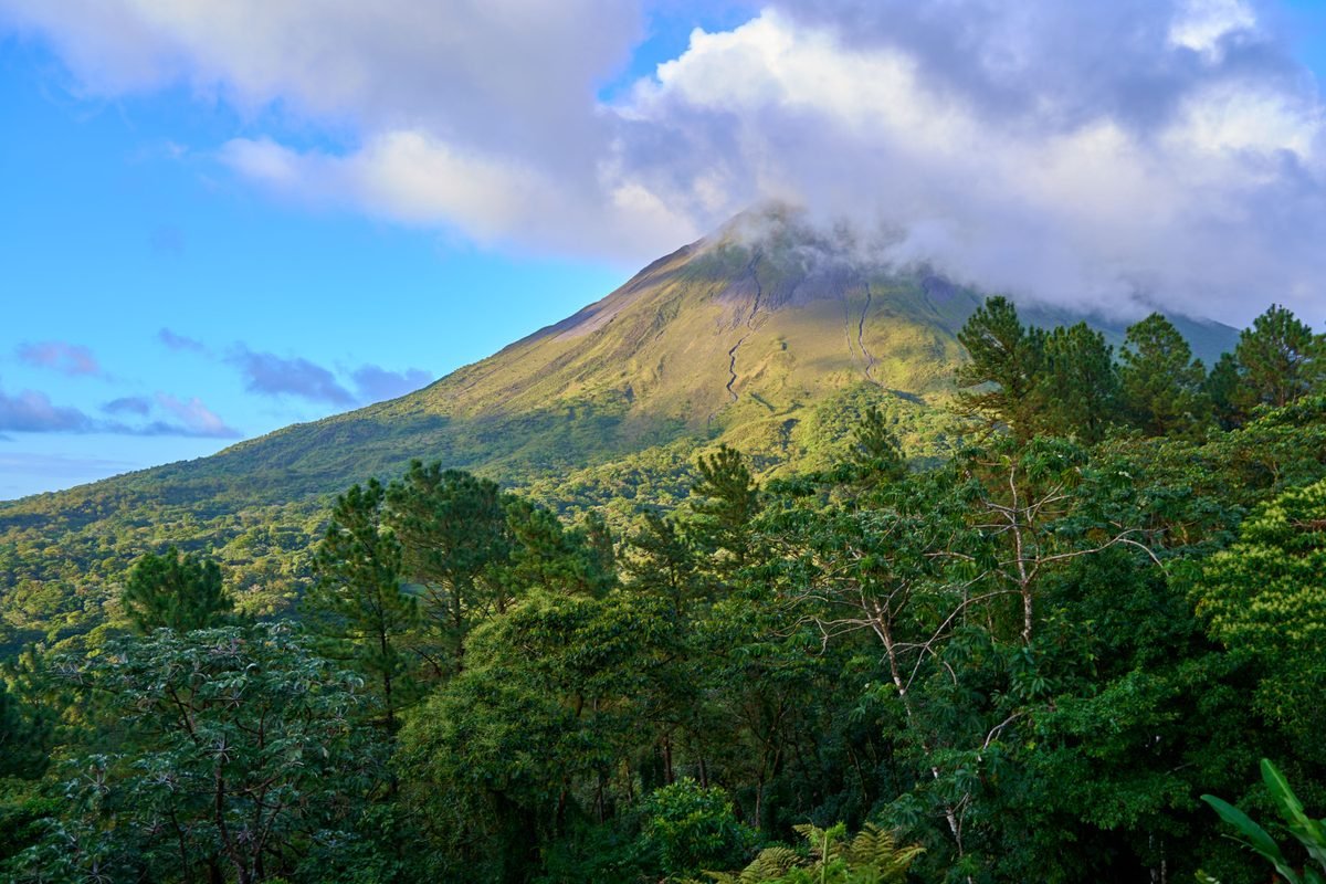 Arenal volcano peak under a cloudy sky with forest in the foreground