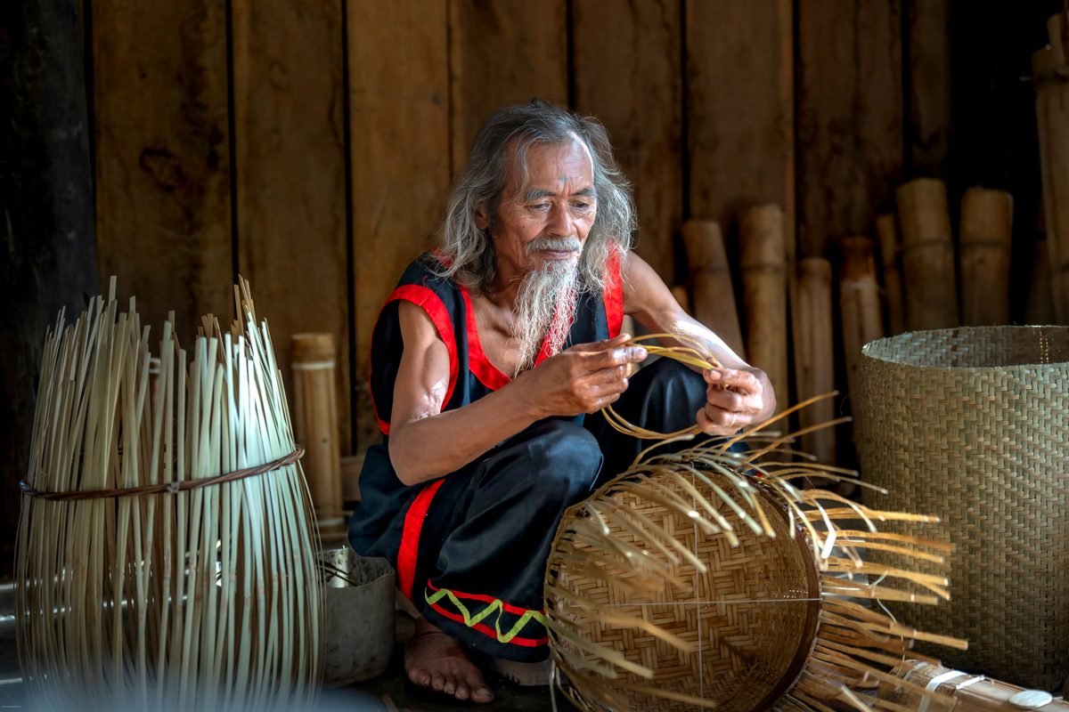 An elderly artisan skillfully weaving bamboo baskets in a traditional setting.