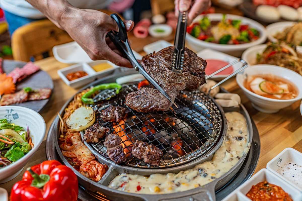 Grilling meat at a Korean barbecue dinner table with various side dishes.