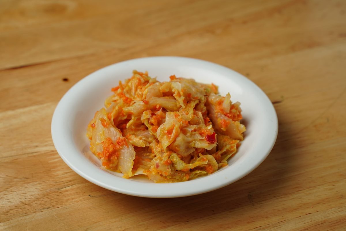 Savory Korean kimchi served in a white bowl on a wooden surface.