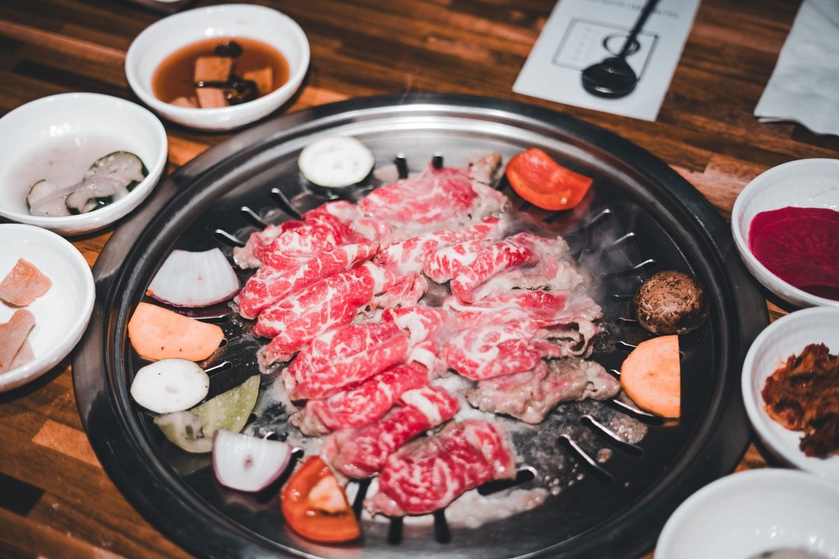 Marbled beef slices grilling on a Korean barbecue table with small side dishes