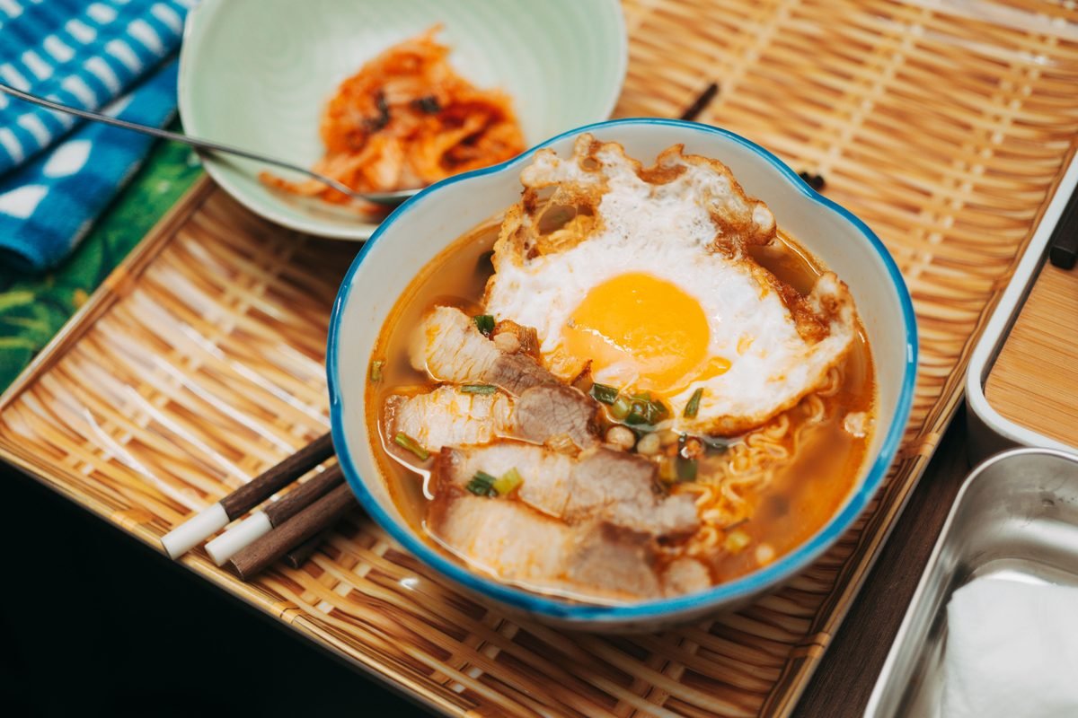 A bowl of spicy ramen topped with a fried egg and served with kimchi.