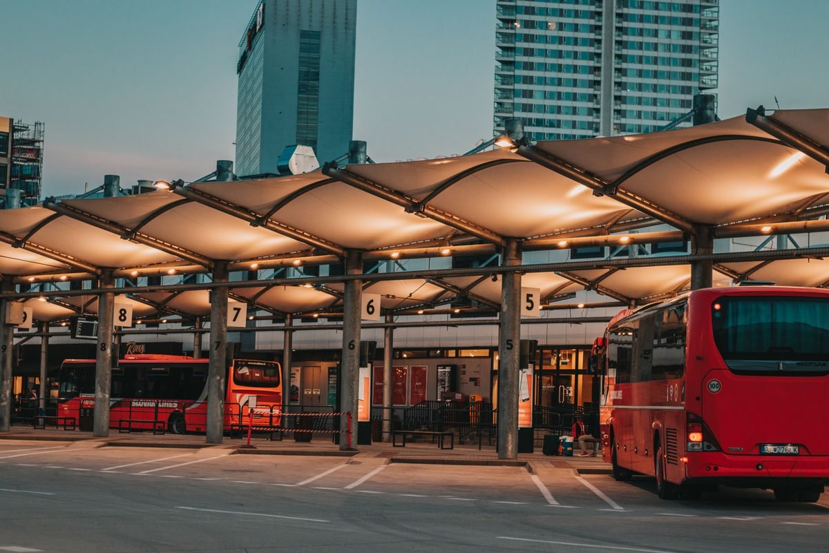 An illuminated bus station with red buses parked under a canopy at dusk.