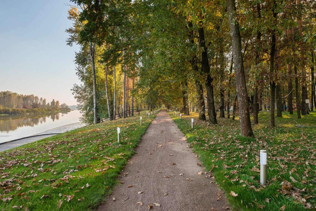 Gravel walking path alongside a calm river lined with autumn trees