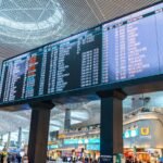 A large digital international departures board in a busy airport terminal.