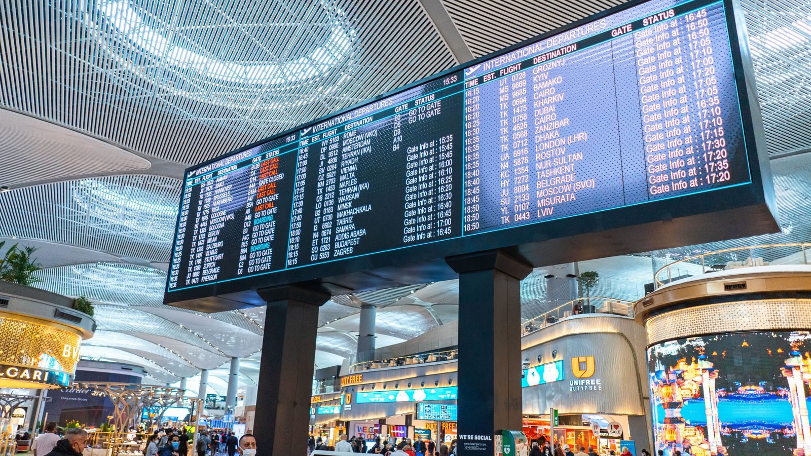 A large digital international departures board in a busy airport terminal.