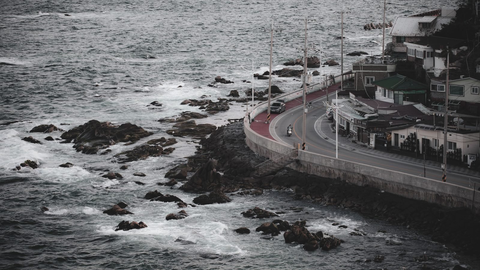 Aerial view of a coastal road and town in Gangneung with rocky shore and sea