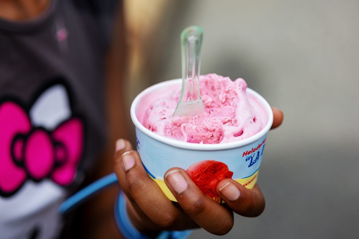 Hand holding a cup of pink gelato with a spoon