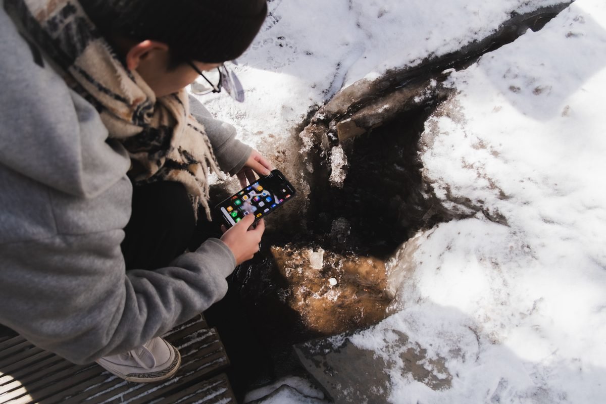 Person examining a smartphone near a snowy stream.