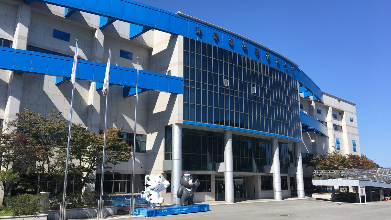 Exterior view of Gangneung Gymnasium with blue framing and Olympic mascots.