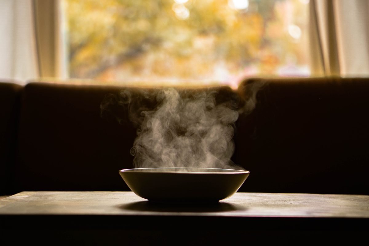 Steaming bowl of hot soup on a wooden table indoors