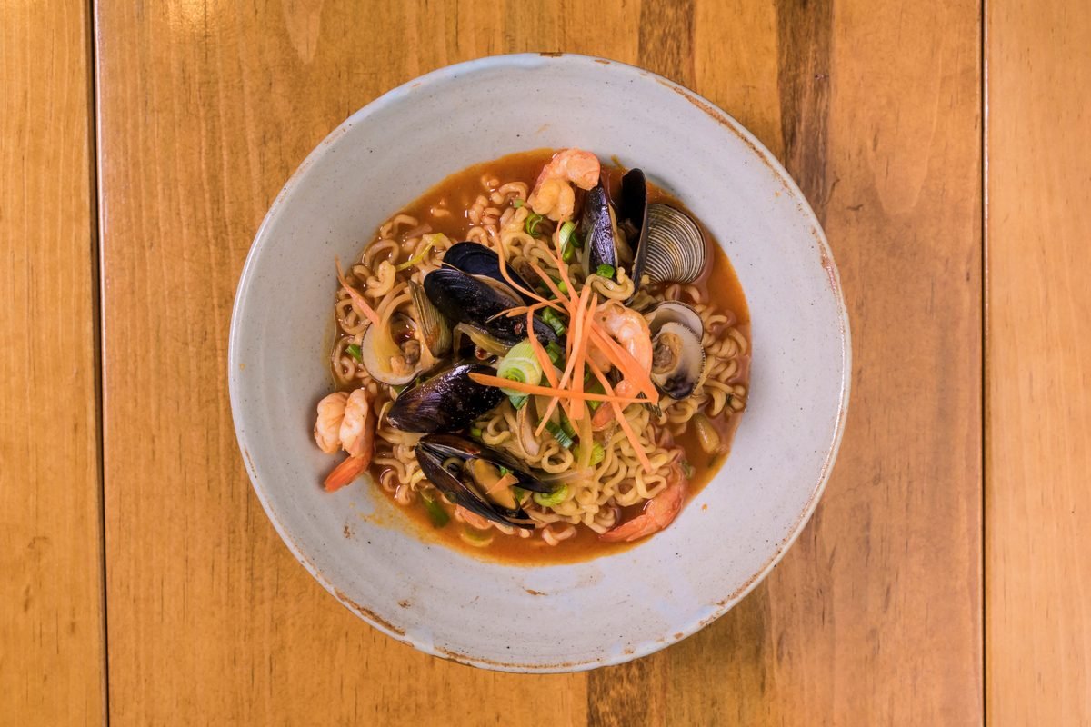 Steaming bowl of spicy seafood noodle soup with mussels and shrimp on wooden table