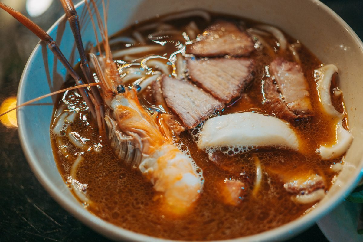 Rich broth seafood noodle soup served in a ceramic bowl with prawn and pork