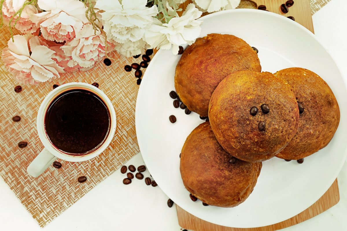 Round golden pastries served on a white plate with coffee and flowers