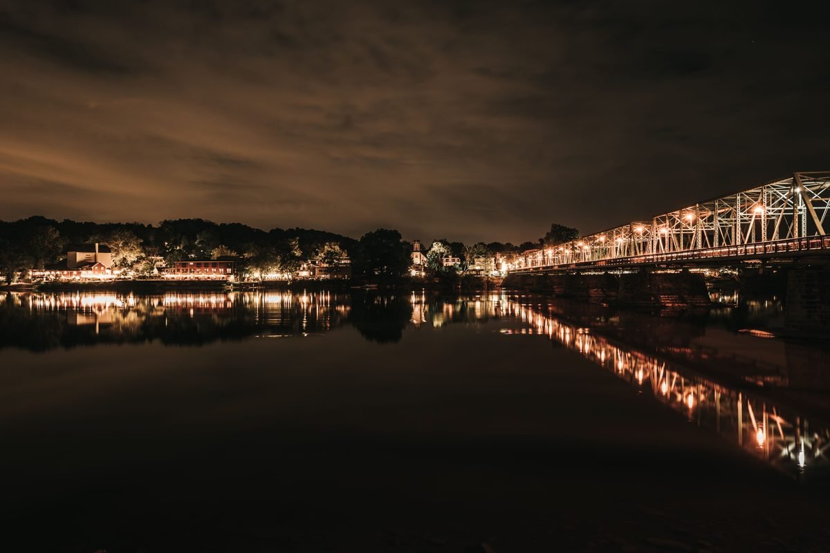 Nighttime cityscape with a lit bridge reflecting on a calm river