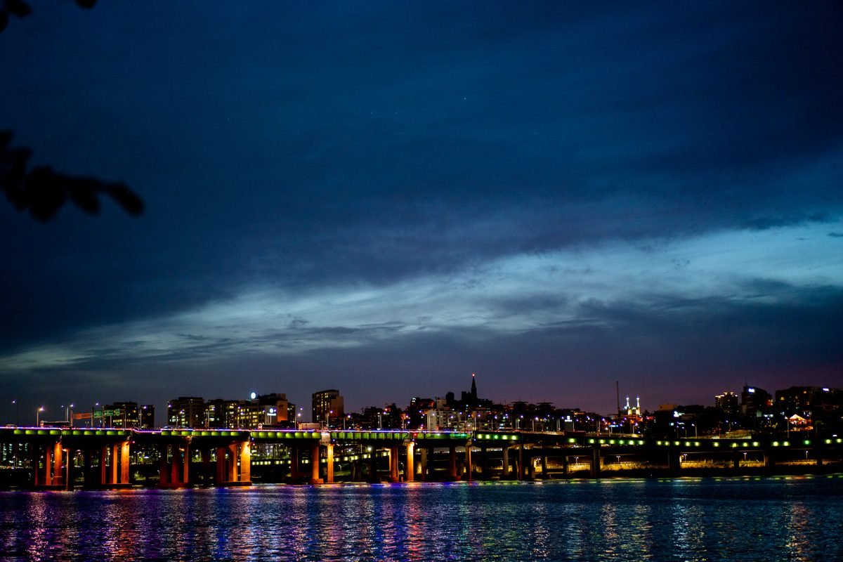 Vibrant cityscape featuring a brightly lit bridge over a river at dusk