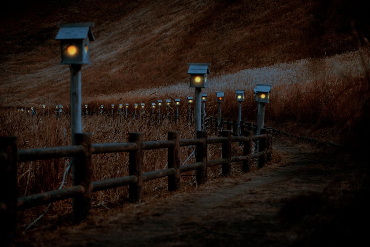 Illuminated stone trail winding past large grassy mounds at dusk