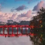 The red Huc Bridge reflecting in the calm green water of Hoan Kiem Lake at twilight in Hanoi